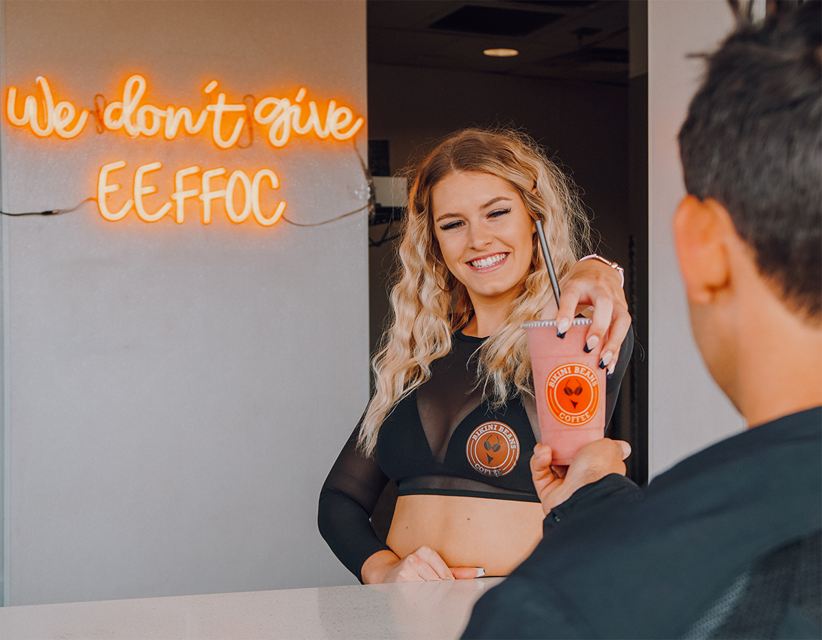 bikini barista handing a smoothie to a customer at coffee stand window